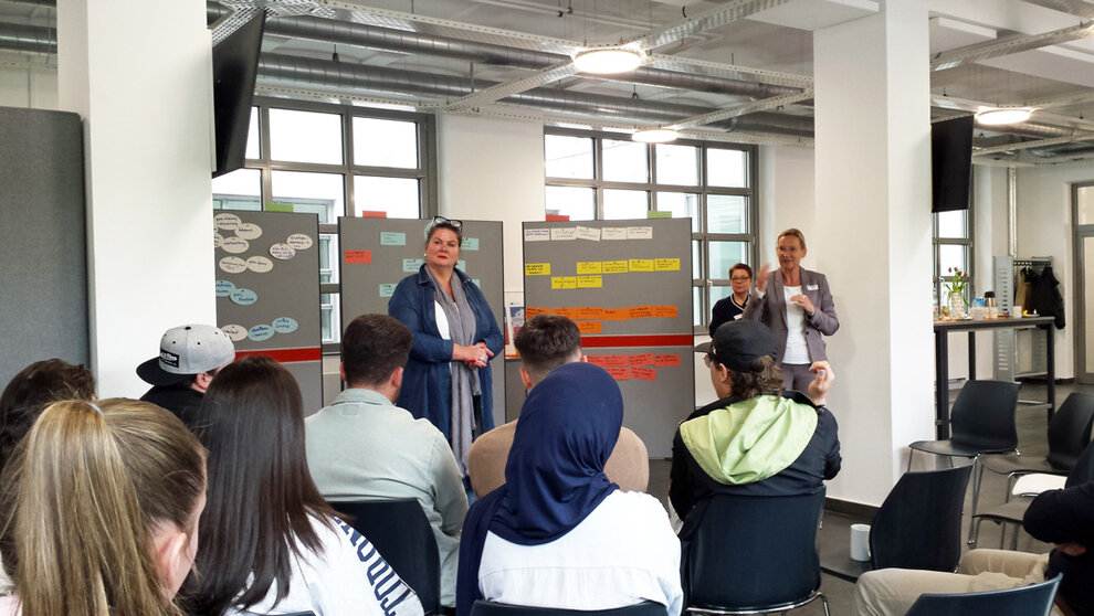 Foto: Teilnehmerinnen und Teilnehmer des 1. Hagener Ausbildungsdialogs.
Moderatorinnen v. l.n.r.: Katja Heck, Vorsitzende der Geschäftsführung der Agentur für Arbeit Hagen, und Michaela Trzecinski, Leiterin der Kommunalen Koordinierung bei der agentur mark GmbH. Im Hintergrund: Iris Rogge-Kaiser, agentur mark.
hagener_ausbildungsdialog_w